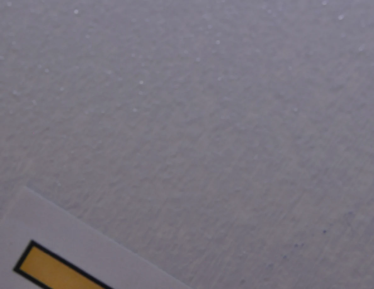 Soft-focus close view of pale textured paint beside a partially cropped yellow label.