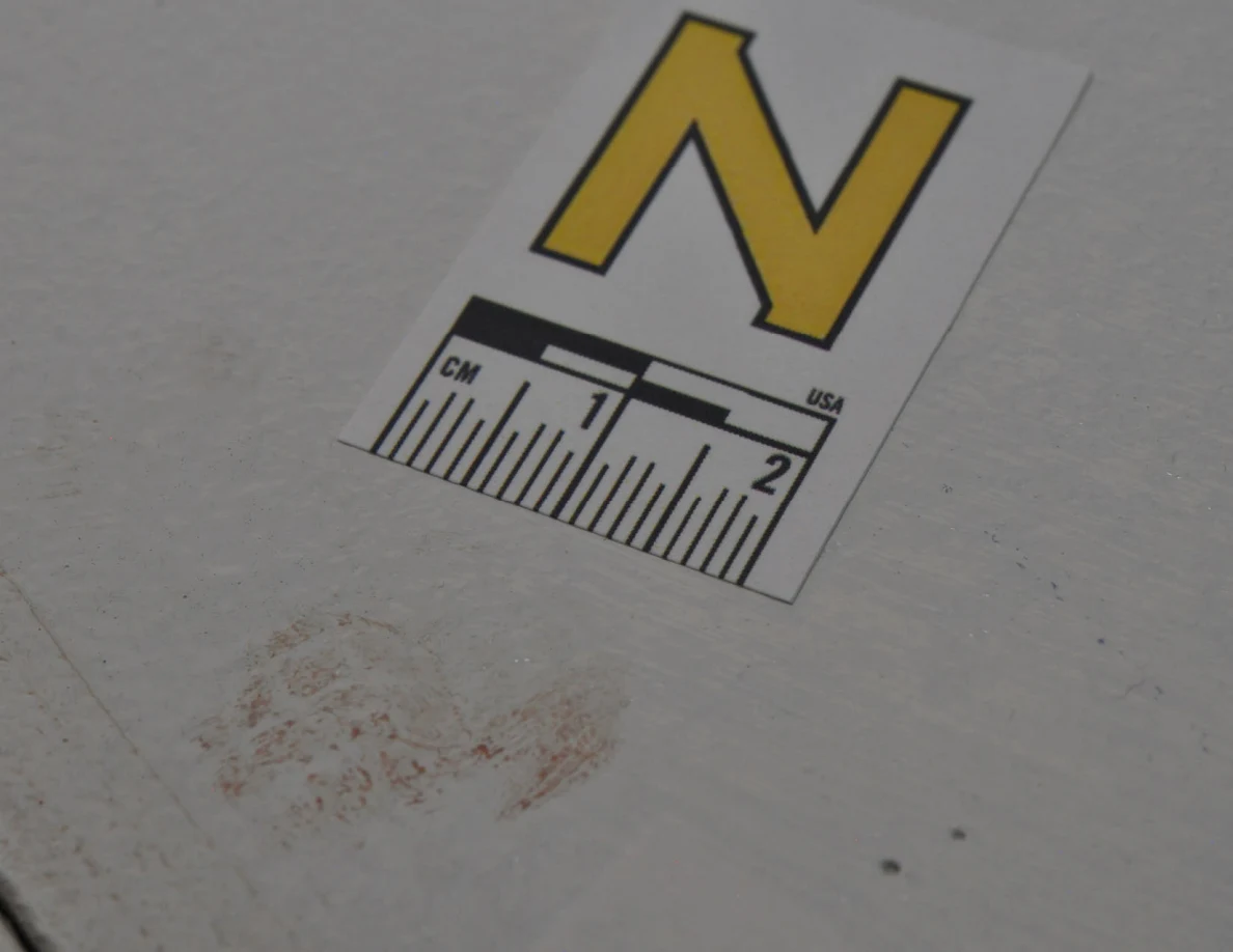 Letter N beside a curved reddish smear on pale paint.