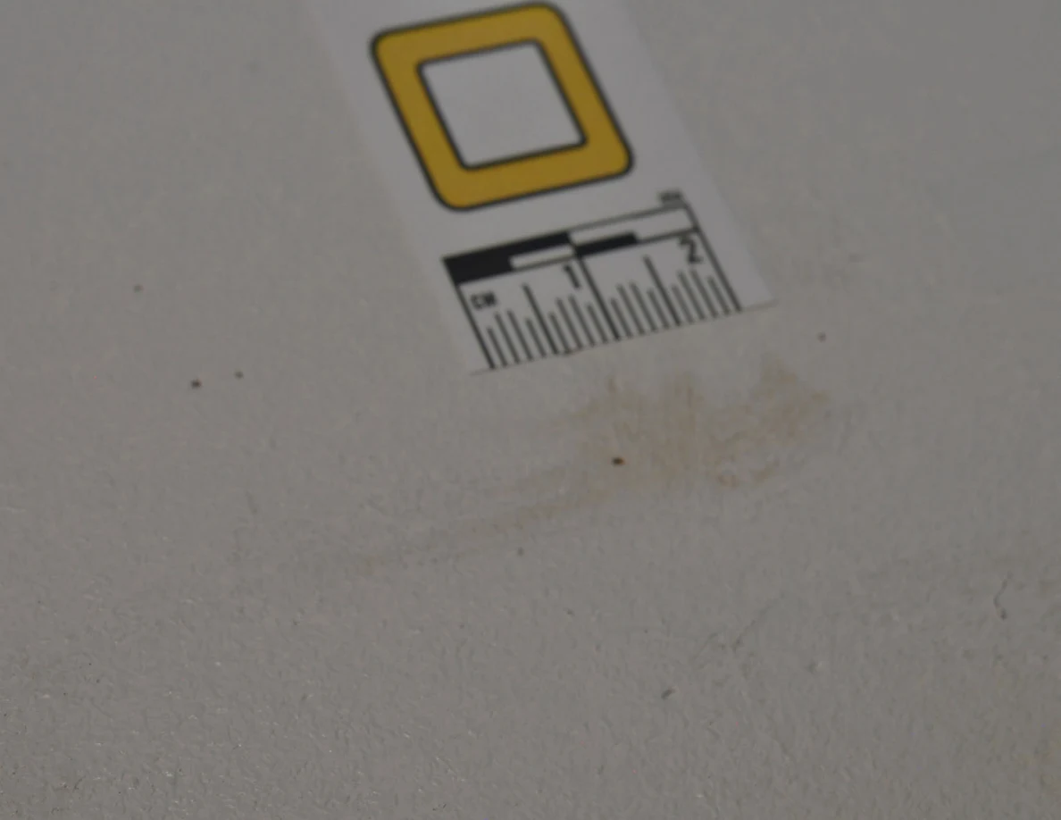 Letter O beside a faint brownish patch on pale paint.