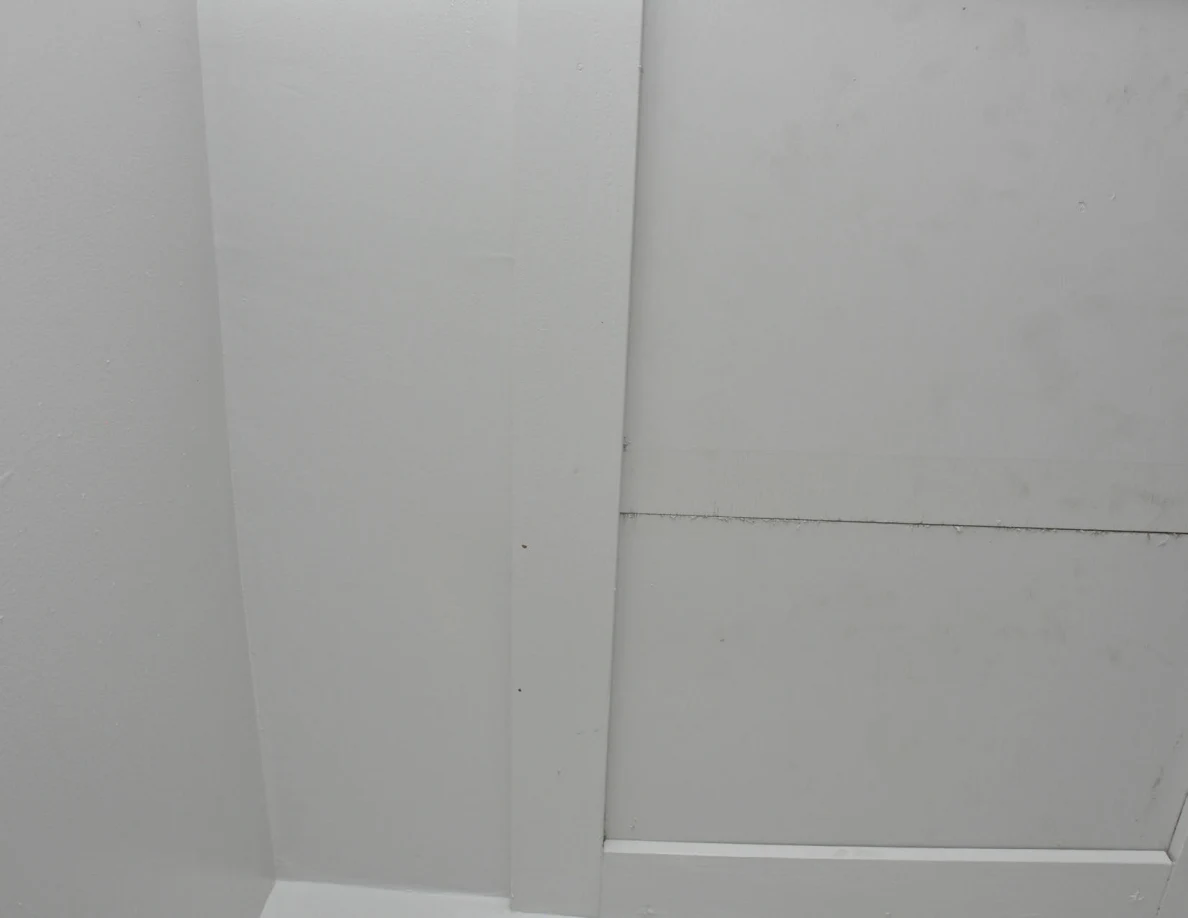Pale wall corner and white horizontal trim with small surface marks.