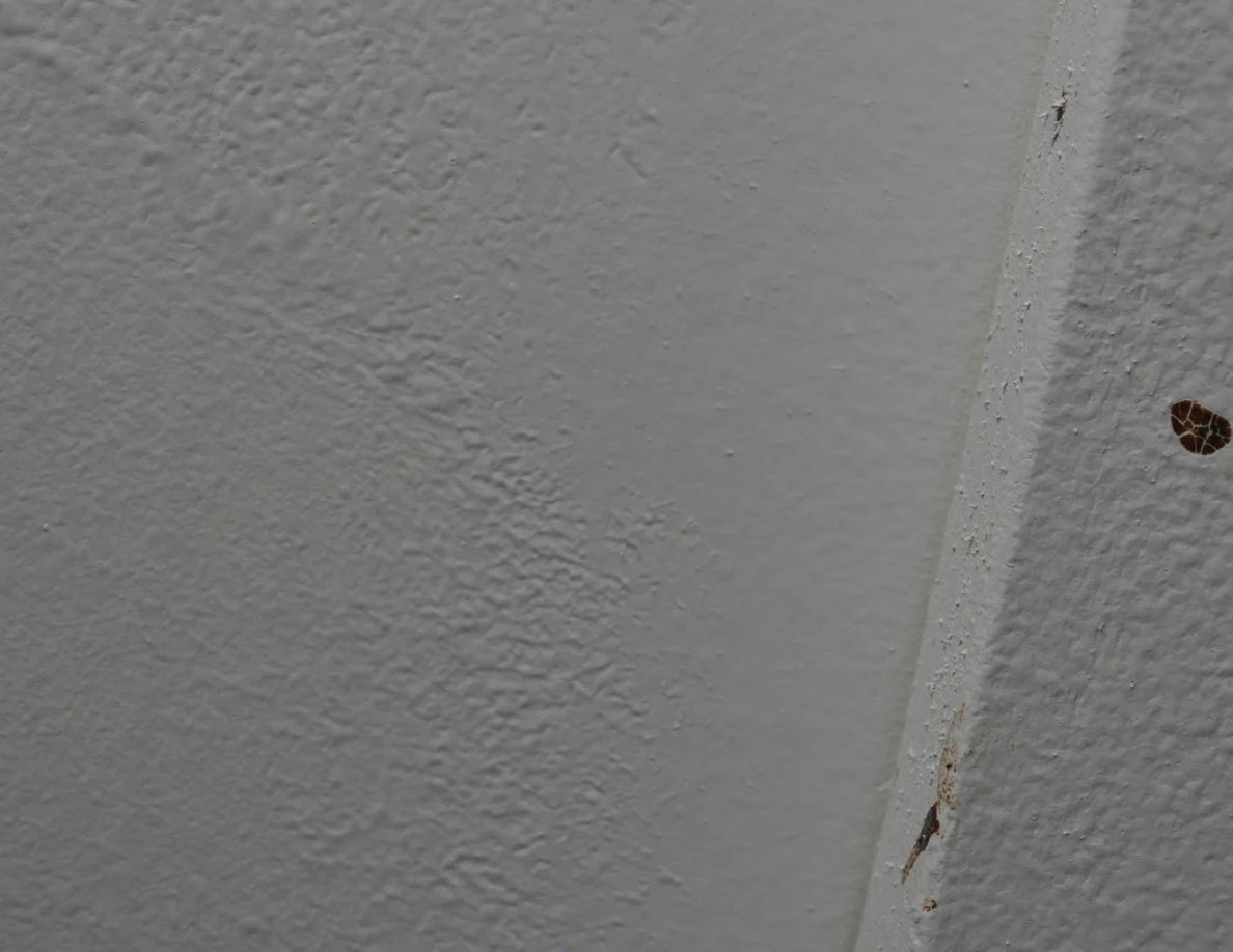 Textured painted corner with a small brown spot at the right edge.
