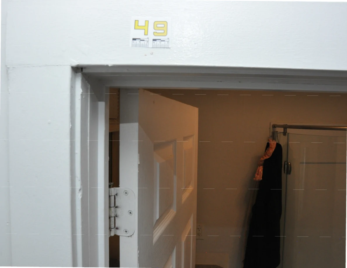 Label 49 on bathroom doorway trim with an open door and a dark garment hanging near a shower.