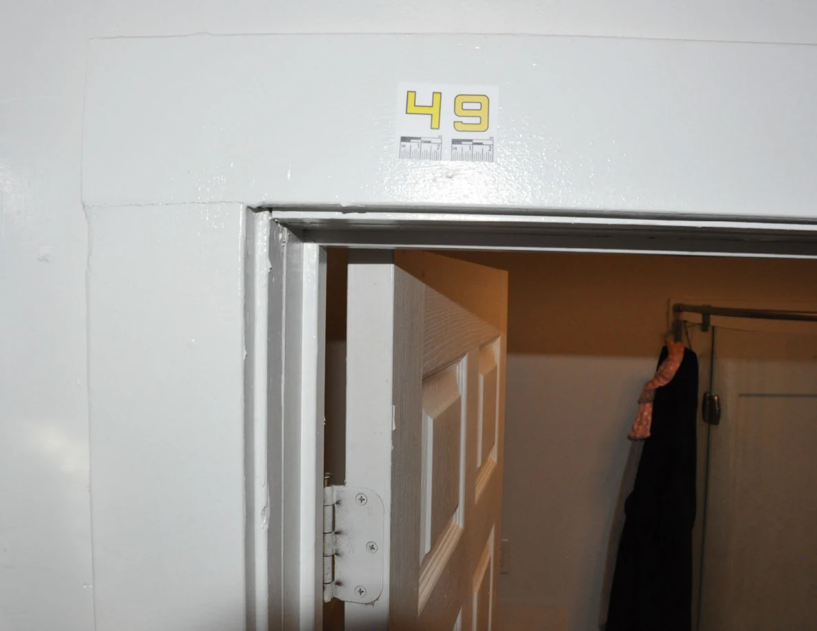White bathroom door frame with label 49, door hinge and shower enclosure beyond.