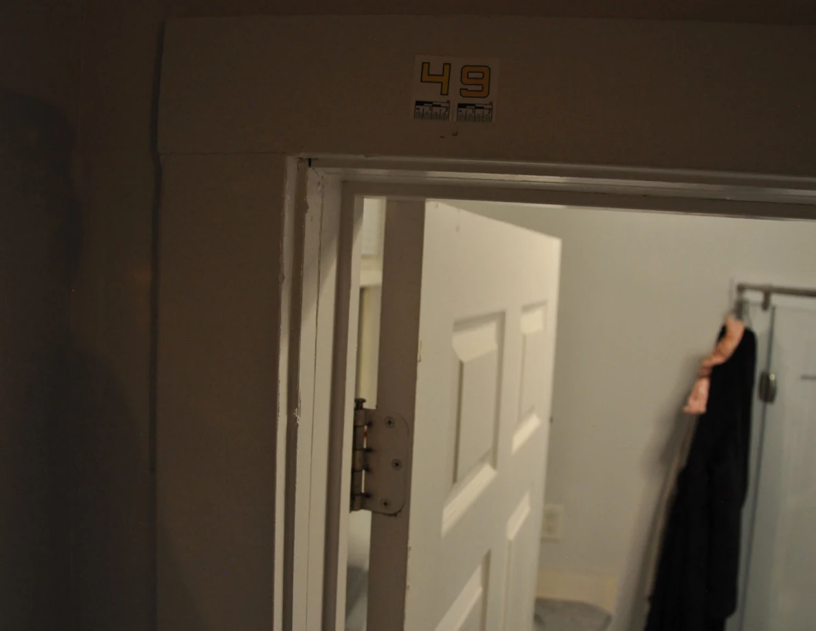 Dim view of label 49 over an open bathroom doorway with a hanging dark garment.