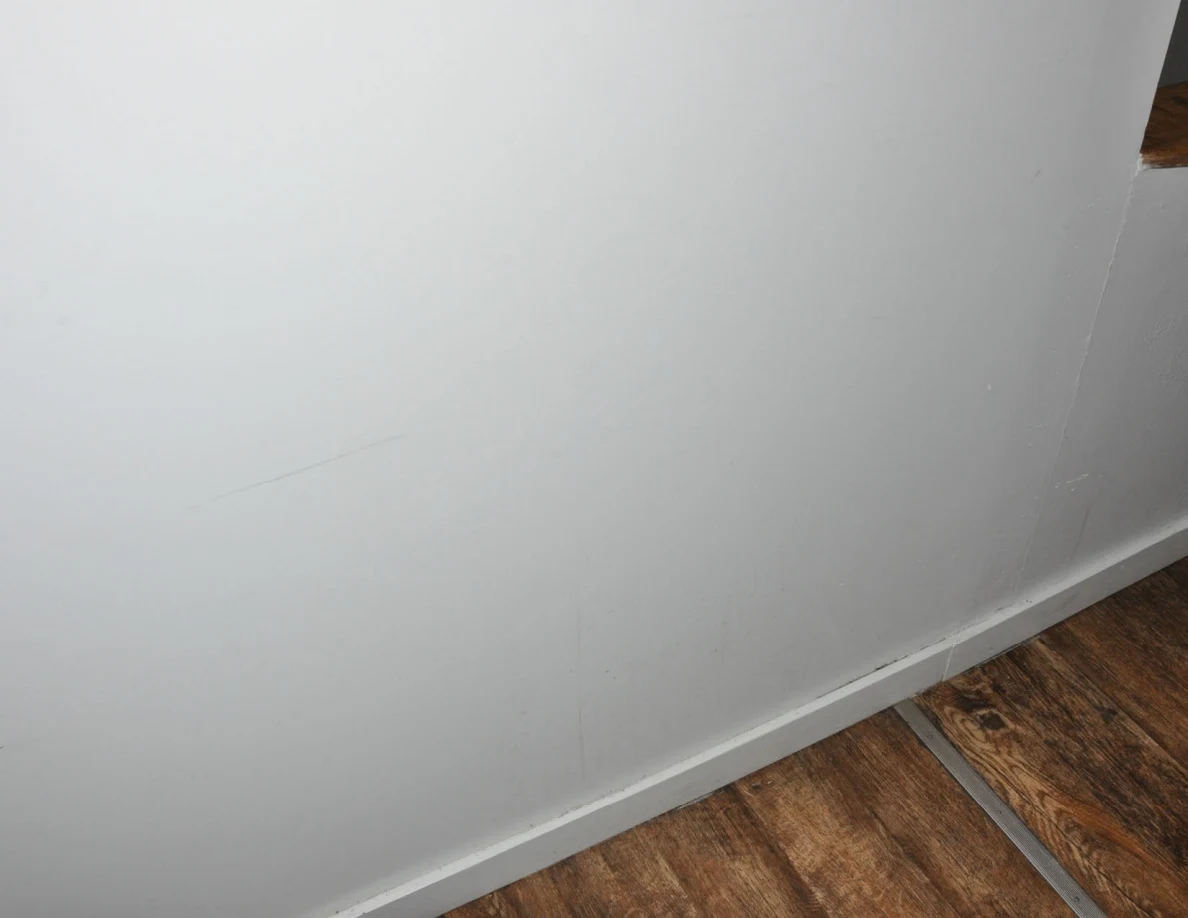 Lower white wall with faint scuff lines above a baseboard and wood-pattern floor.