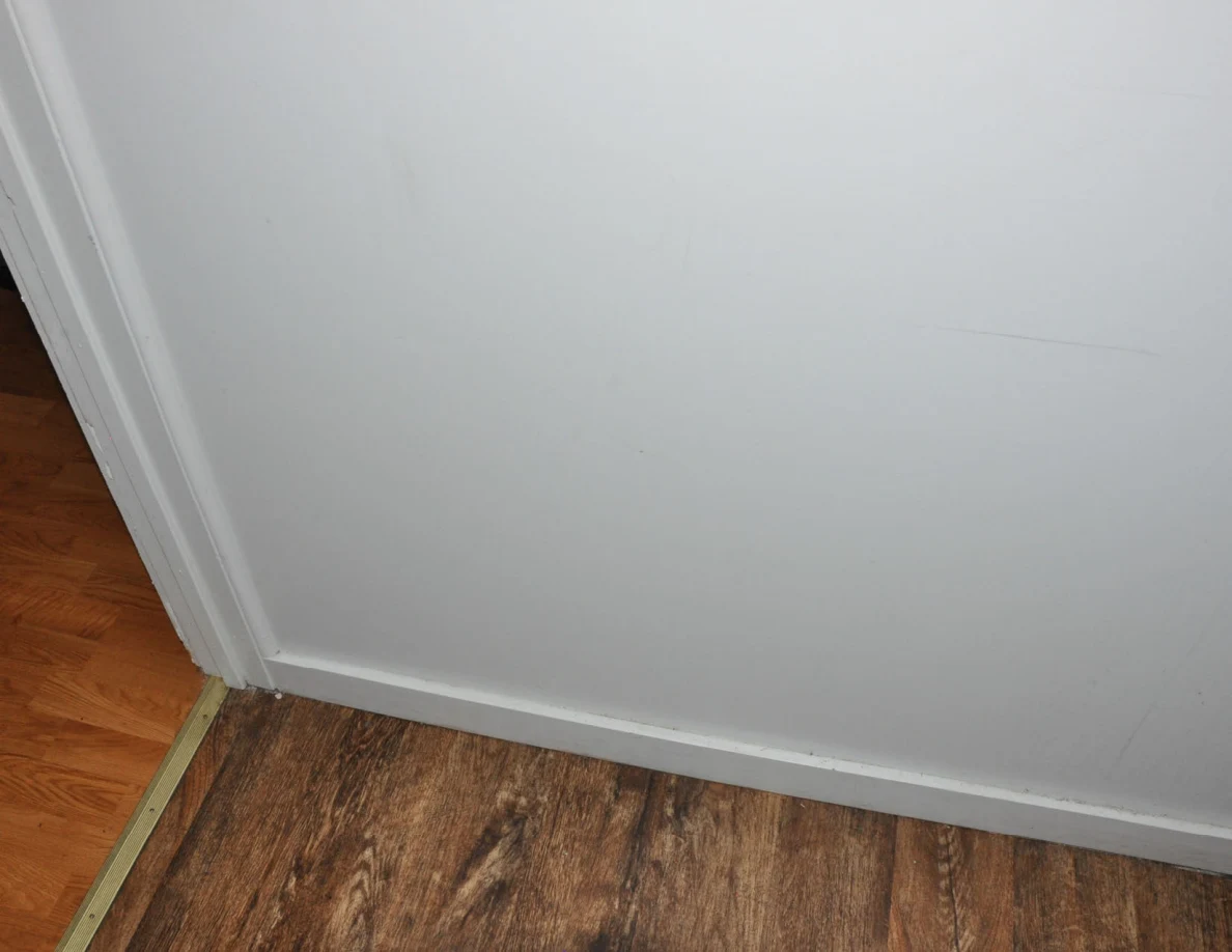 Faint marks on a white wall above baseboard trim beside a doorway threshold.