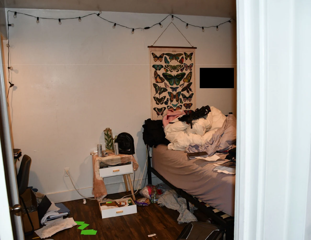 Bedroom with rumpled bedding, butterfly wall hanging, string lights, open bedside drawers and scattered papers; some areas are redacted.