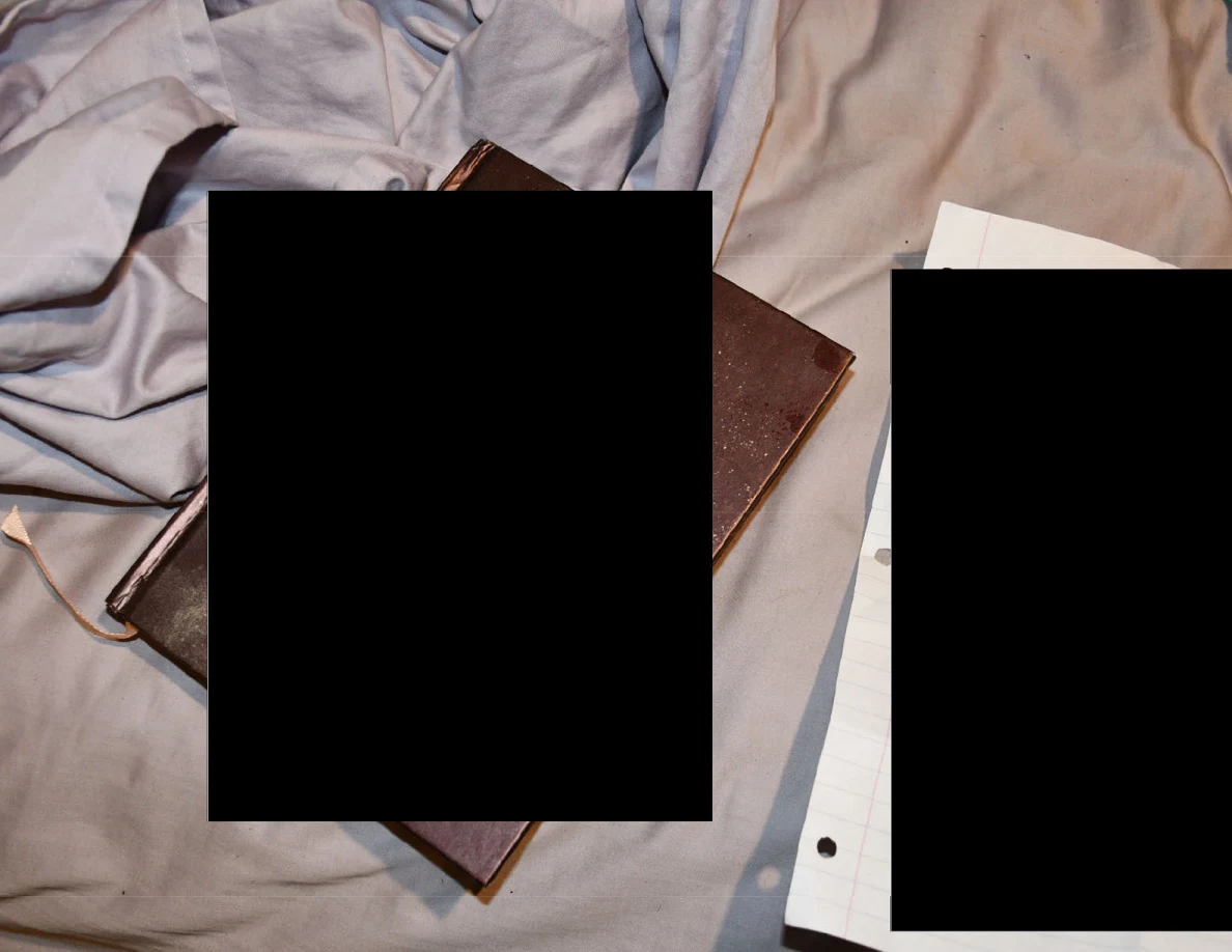 Book and loose papers on bedding with large black redaction blocks.