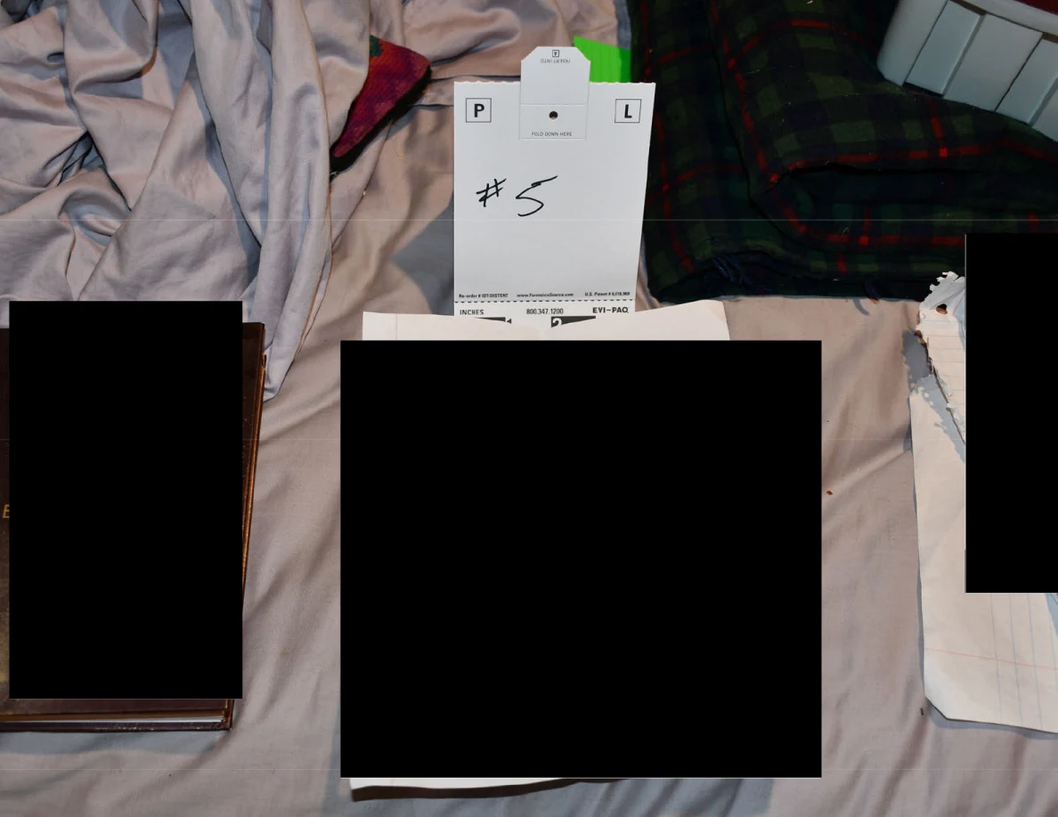 Number 5 scale card beside a journal and redacted papers on bedding.