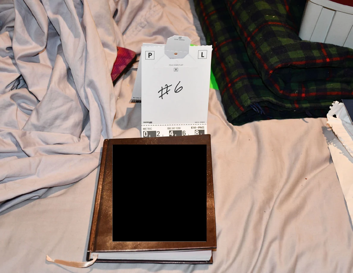 Number 6 scale card above a brown journal with a redacted cover on bedding.