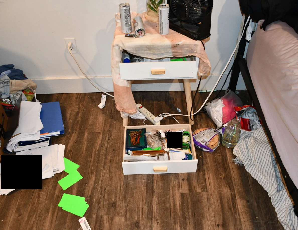 Bedside drawers open above and on the floor among papers, green markers, cables and drink containers.
