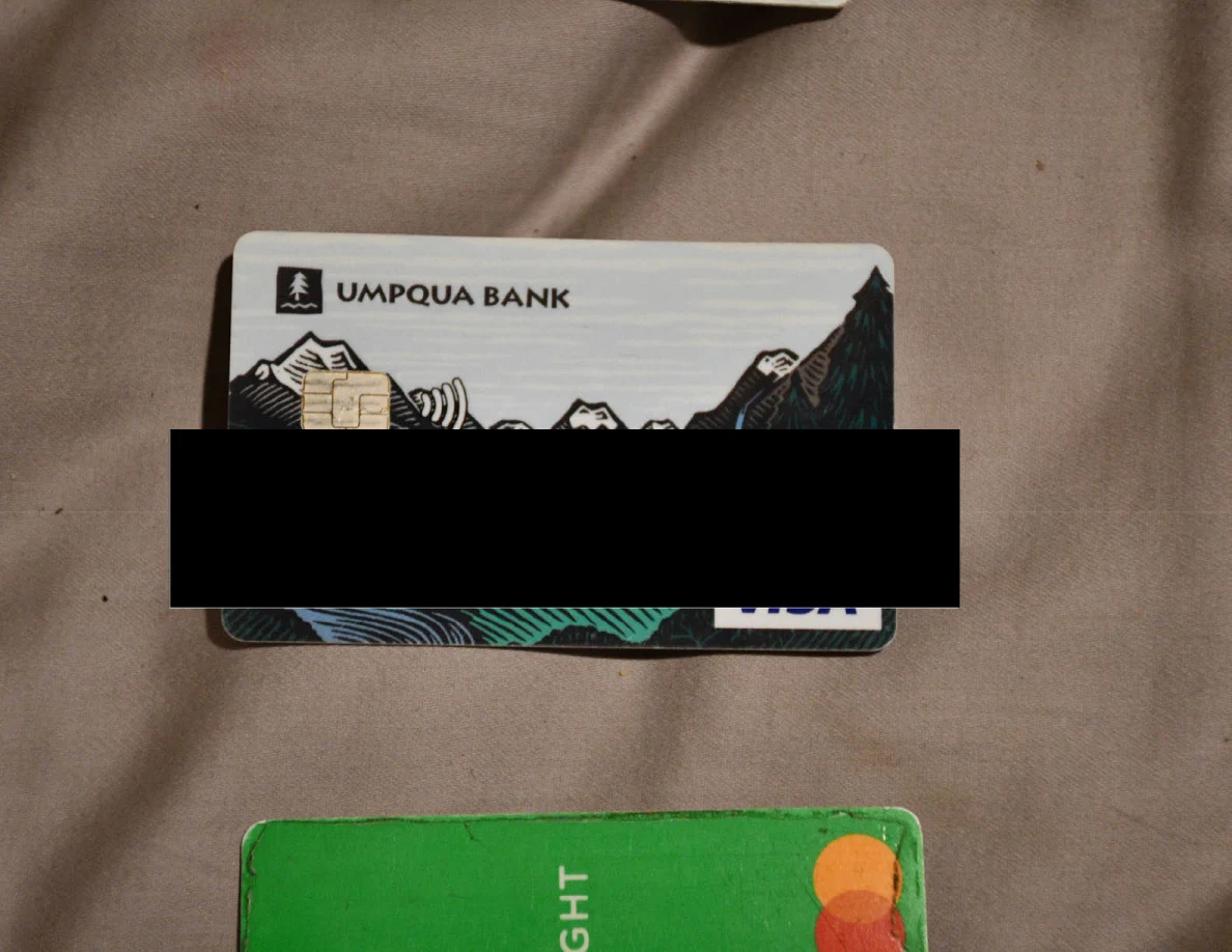 Partly redacted bank card on bedding above the edge of a green card.