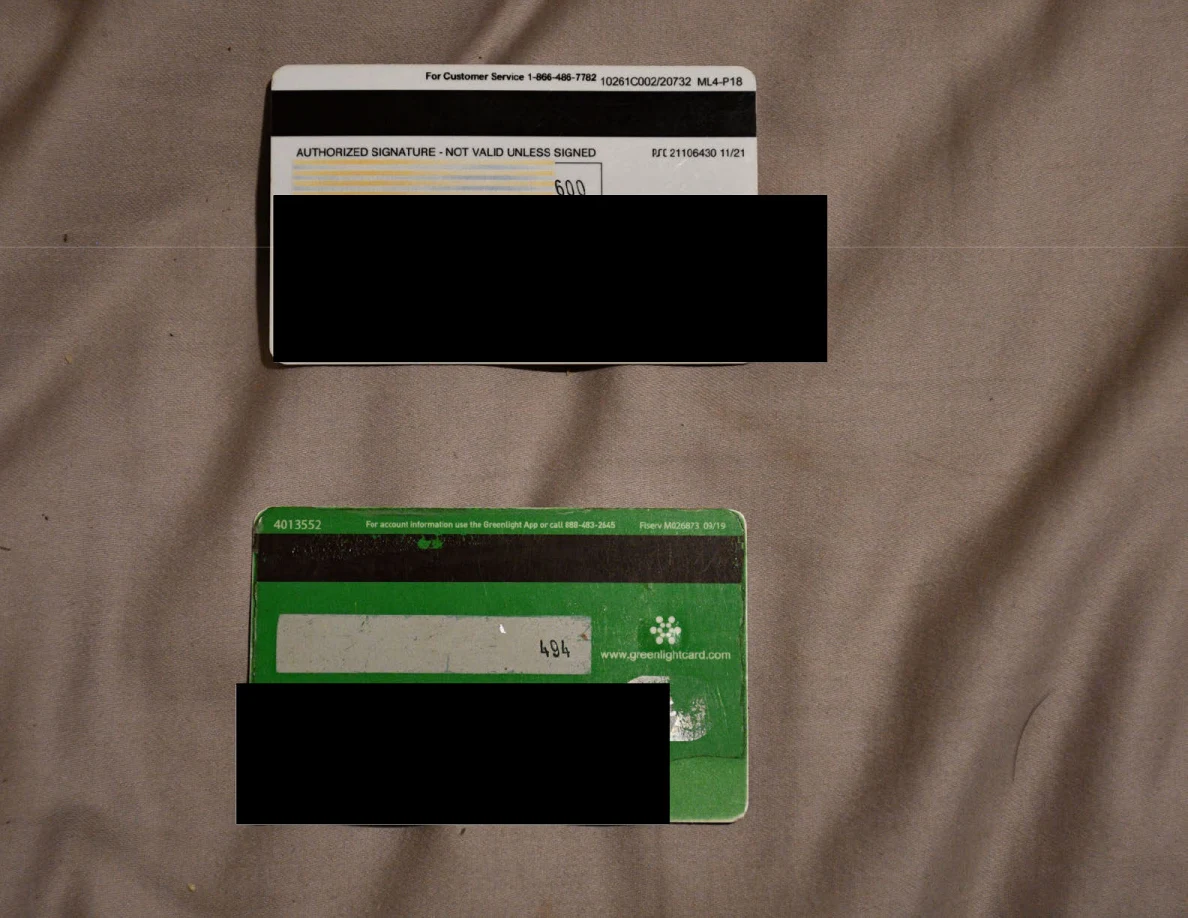 Reverse sides of two cards on bedding with black redactions across details.