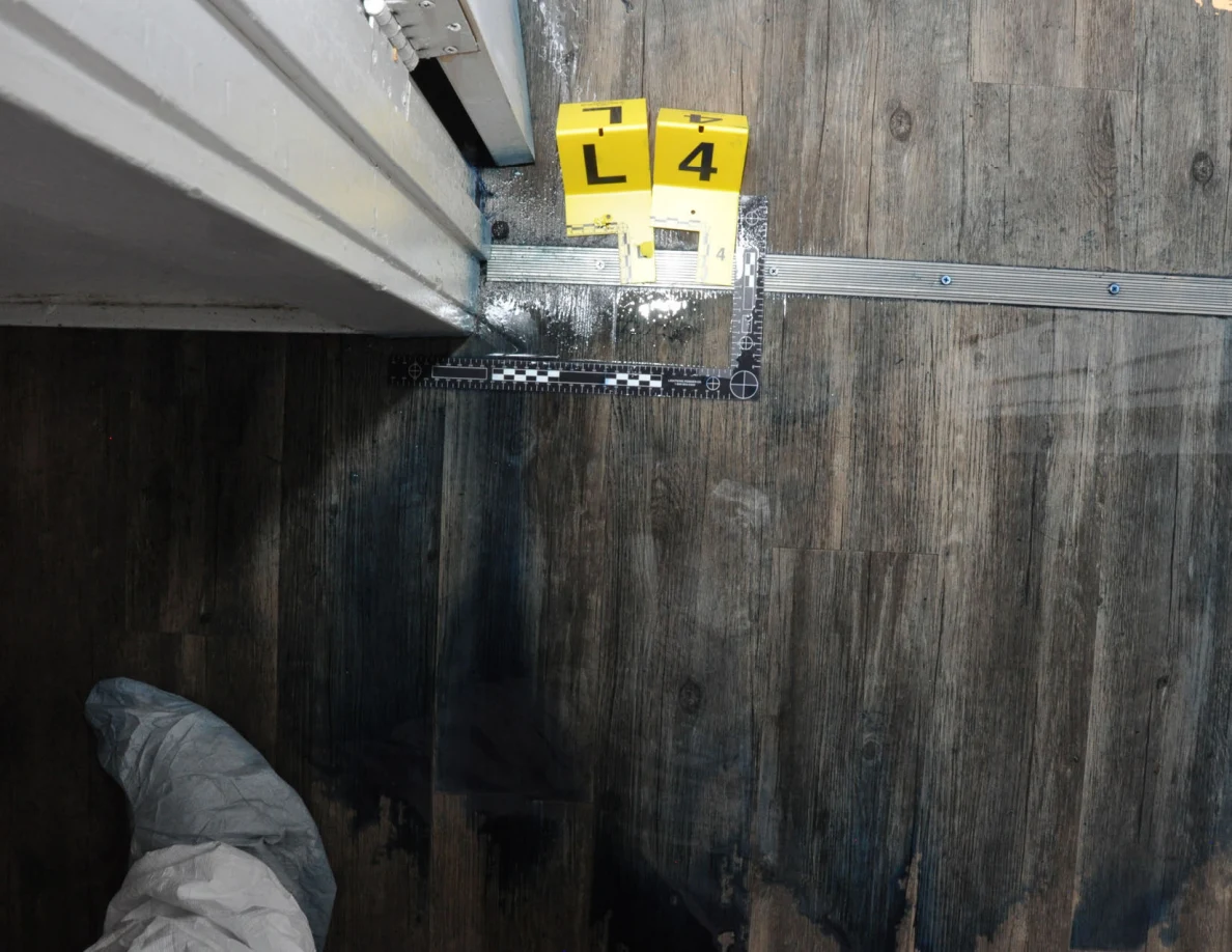 Markers L and 4 beside a metal doorway threshold and an L-shaped measuring scale on wood-pattern flooring.