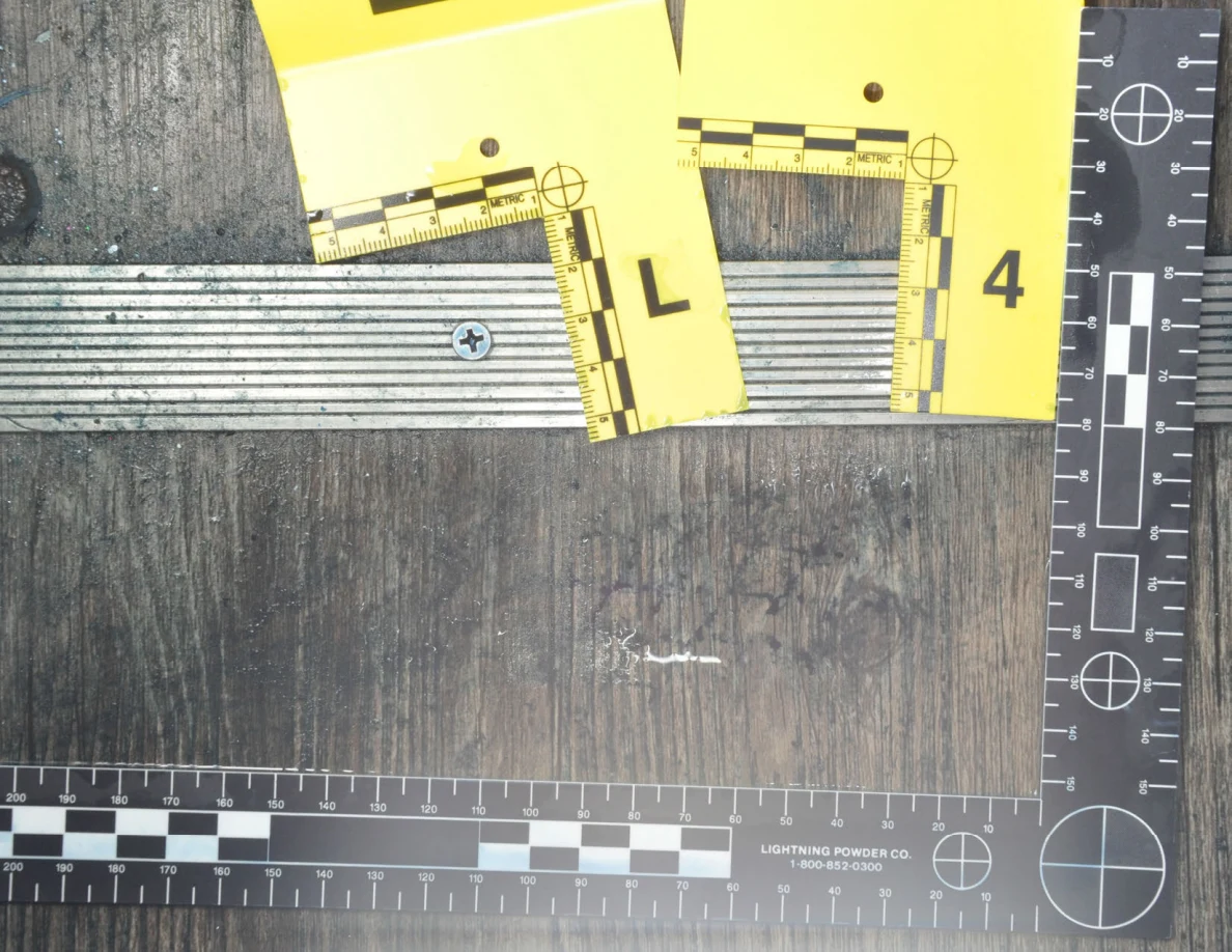 Glare across wood-pattern flooring and dark marks bordered by a black measuring scale.