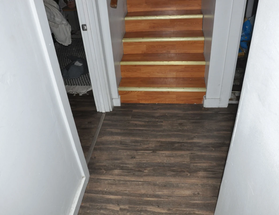 Hall floor facing wooden stairs between two room doorways.