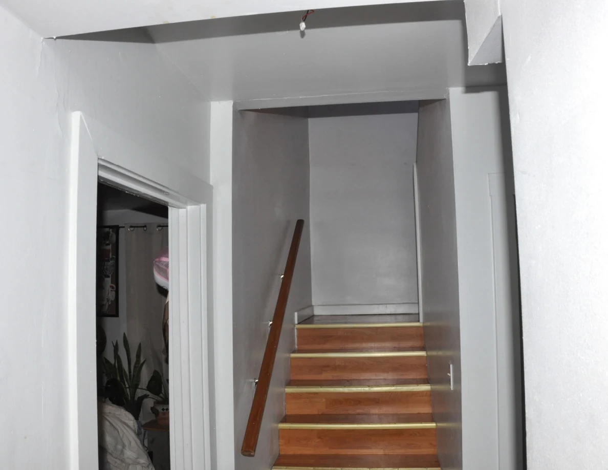 Upper view of the stairwell opening and wooden steps beside an open bedroom.