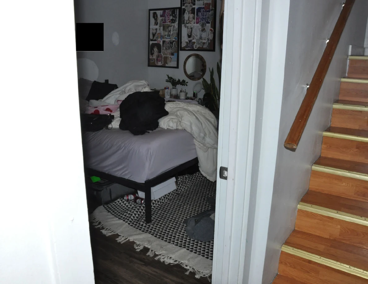 Bed and patterned rug seen through a doorway beside wooden stairs and handrail.