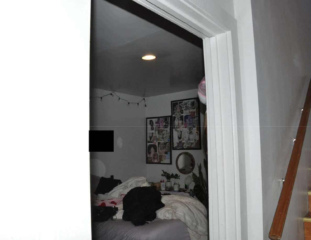 Upper bedroom doorway with a ceiling light, string lights and wall collages above rumpled bedding.
