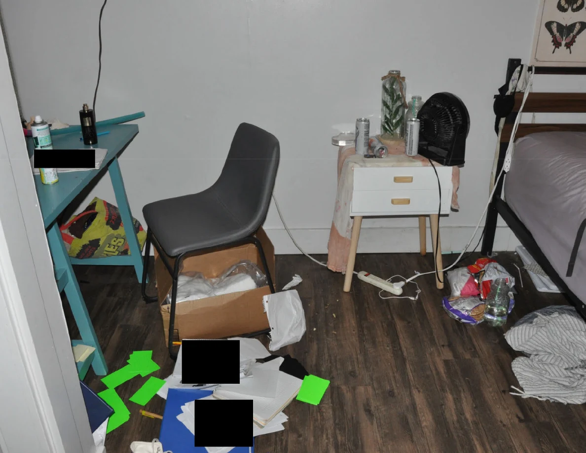 Gray chair beside a turquoise desk and white bedside table, with loose papers, green markers and cables on the floor.