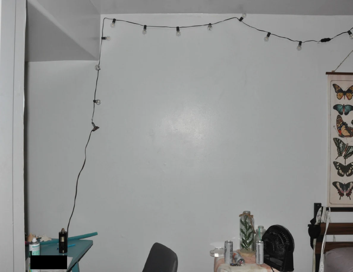 String lights running along a pale bedroom wall above a chair and bedside table.