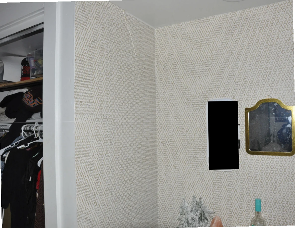 Patterned wall corner with small mirrors beside an open closet containing hanging clothes.