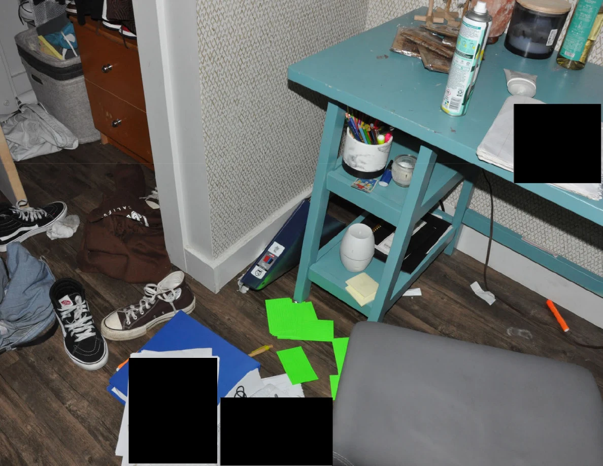 Desk shelving and floor with shoes, green cards, loose papers and redacted areas beside an open closet.
