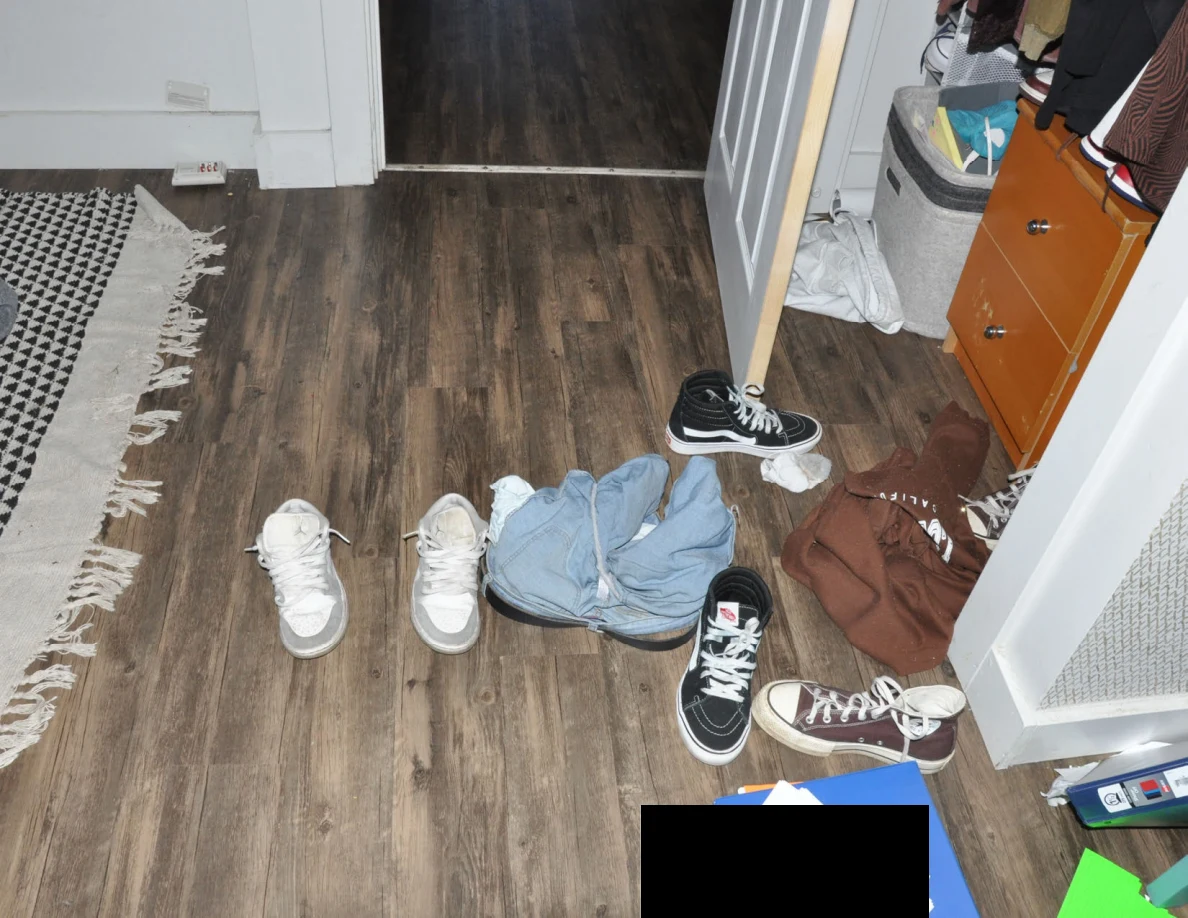 Shoes and loose clothing on a wood-pattern bedroom floor between a rug and open closet.