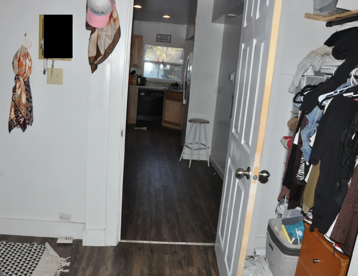 View from a bedroom through an open door toward a kitchen, with hats and scarves hanging beside the doorway.