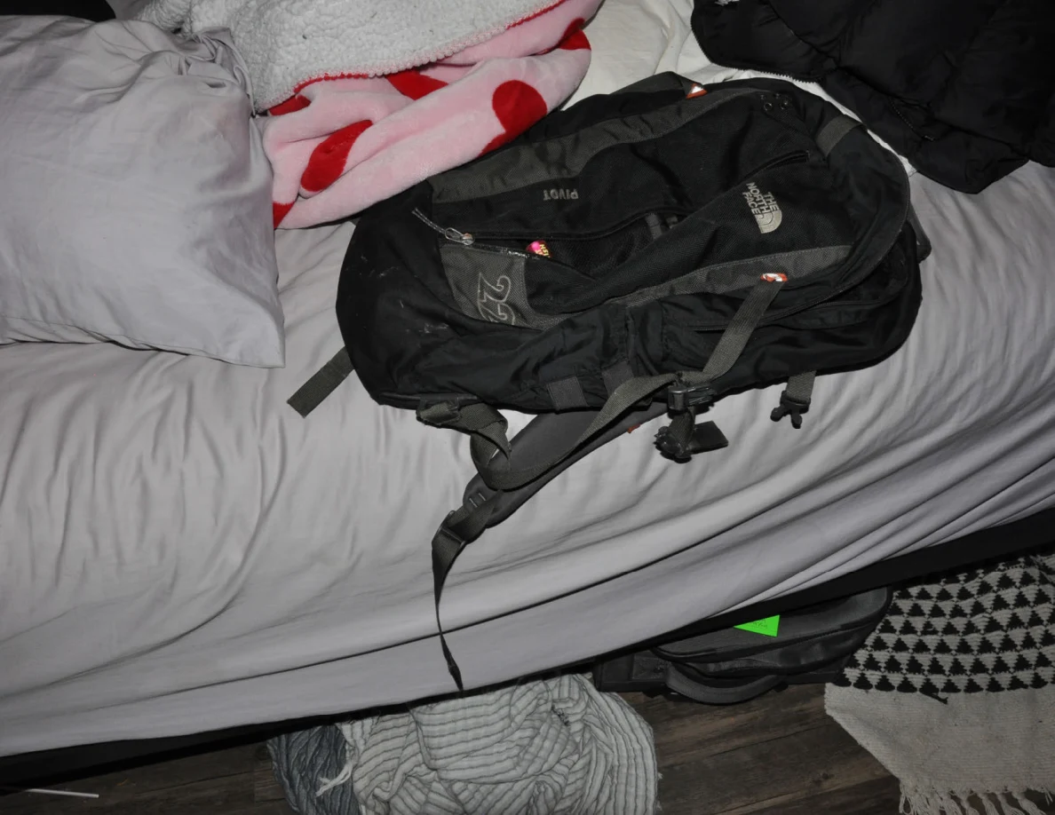 Close view of a black backpack with straps resting on gray bedding.