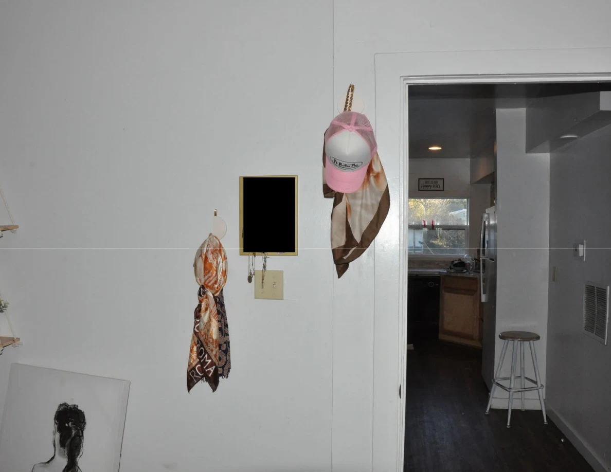 Hats and scarves hanging beside a bedroom doorway that opens toward a kitchen.
