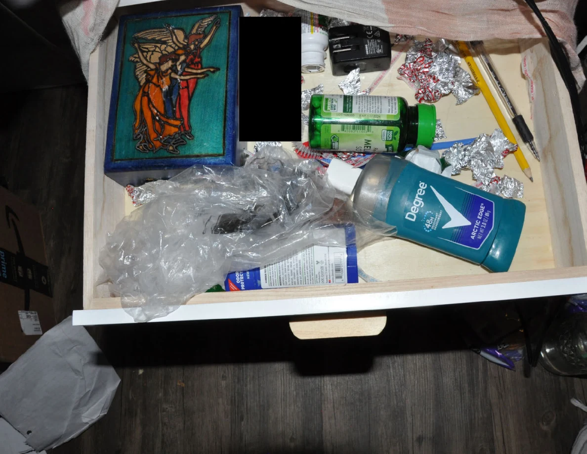Open drawer with toiletries, melatonin bottle, wrappers, plastic bags and a decorative box.