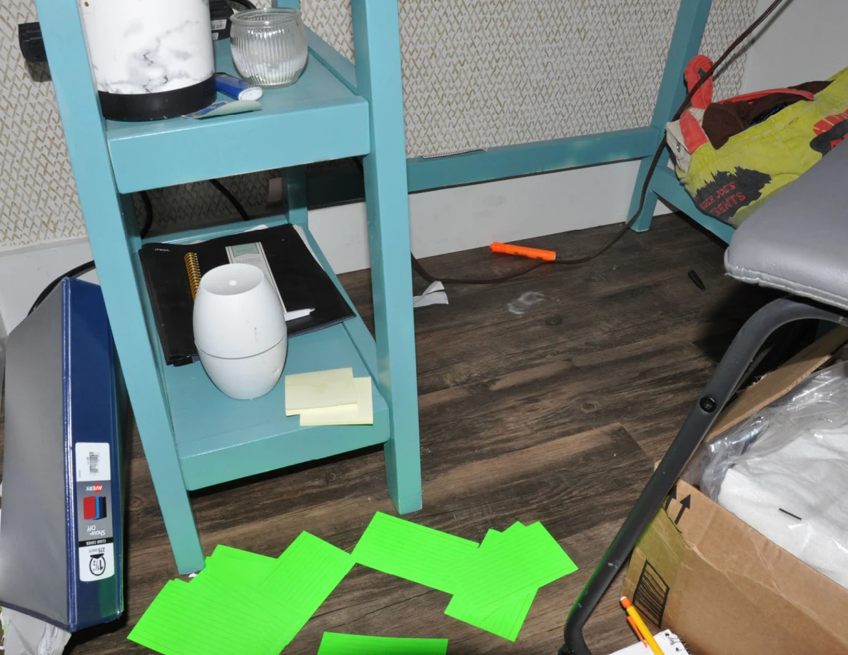 Lower turquoise desk shelving above green cards, cables and small objects on wood-pattern flooring.