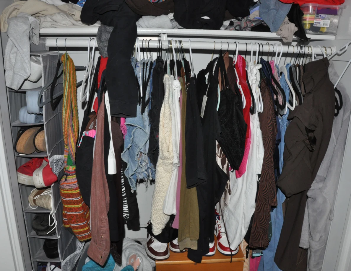 Closet rail crowded with clothes on hangers beside a hanging shoe organizer.