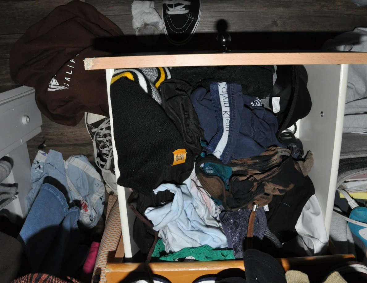 Another open wooden drawer containing folded and loose clothing.