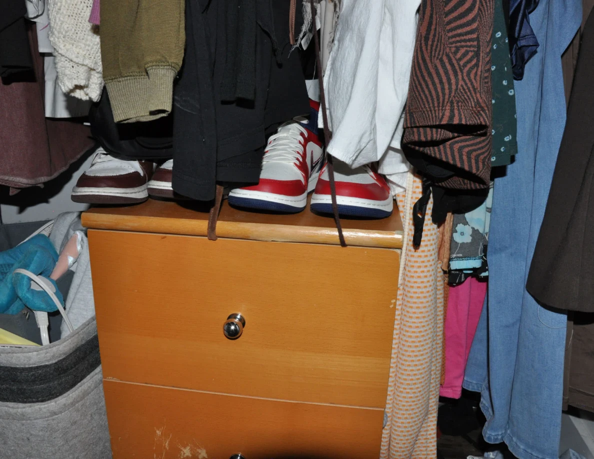 Wooden closet drawers with red-and-white shoes above them and hanging garments.
