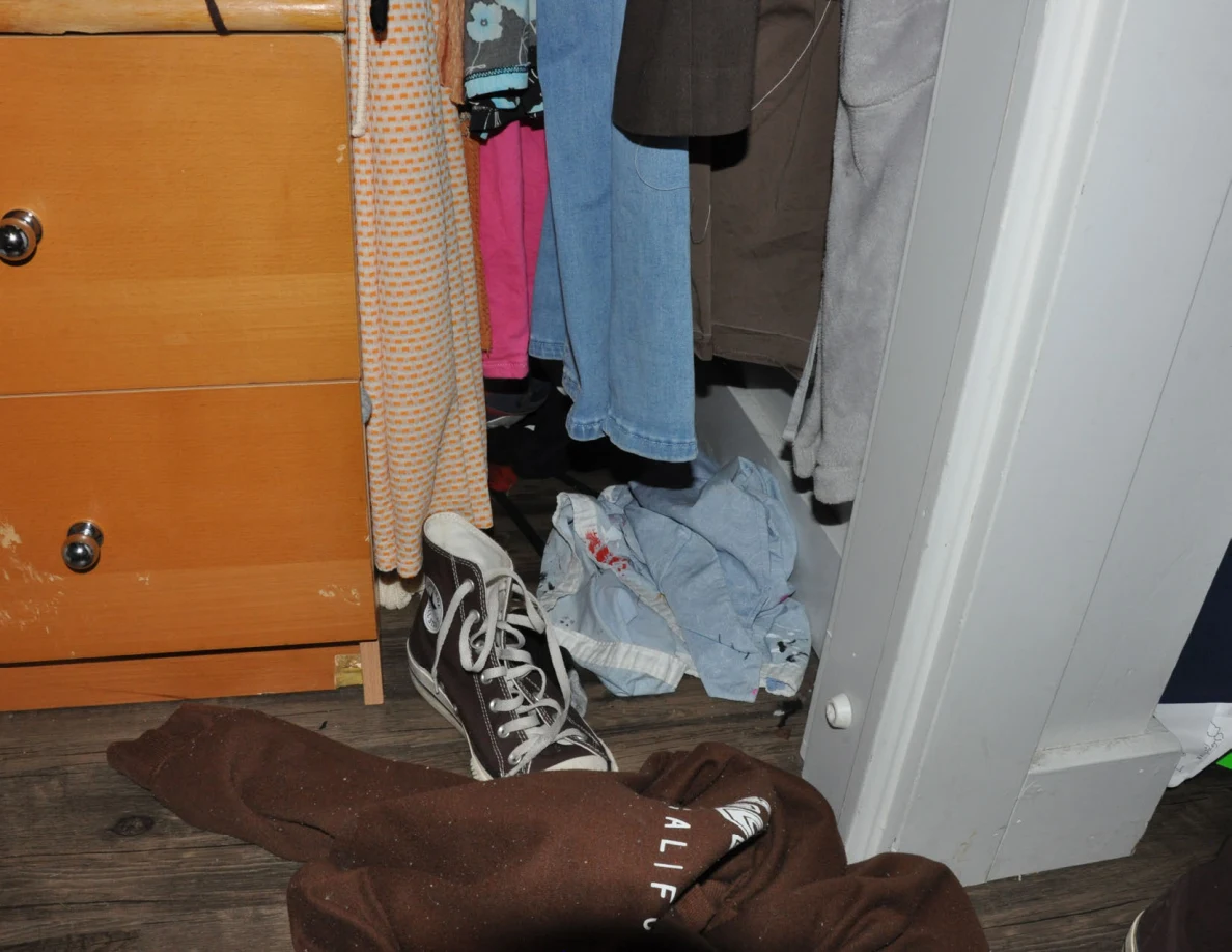 Lower closet corner with shoes and loose clothing beside wooden drawers.