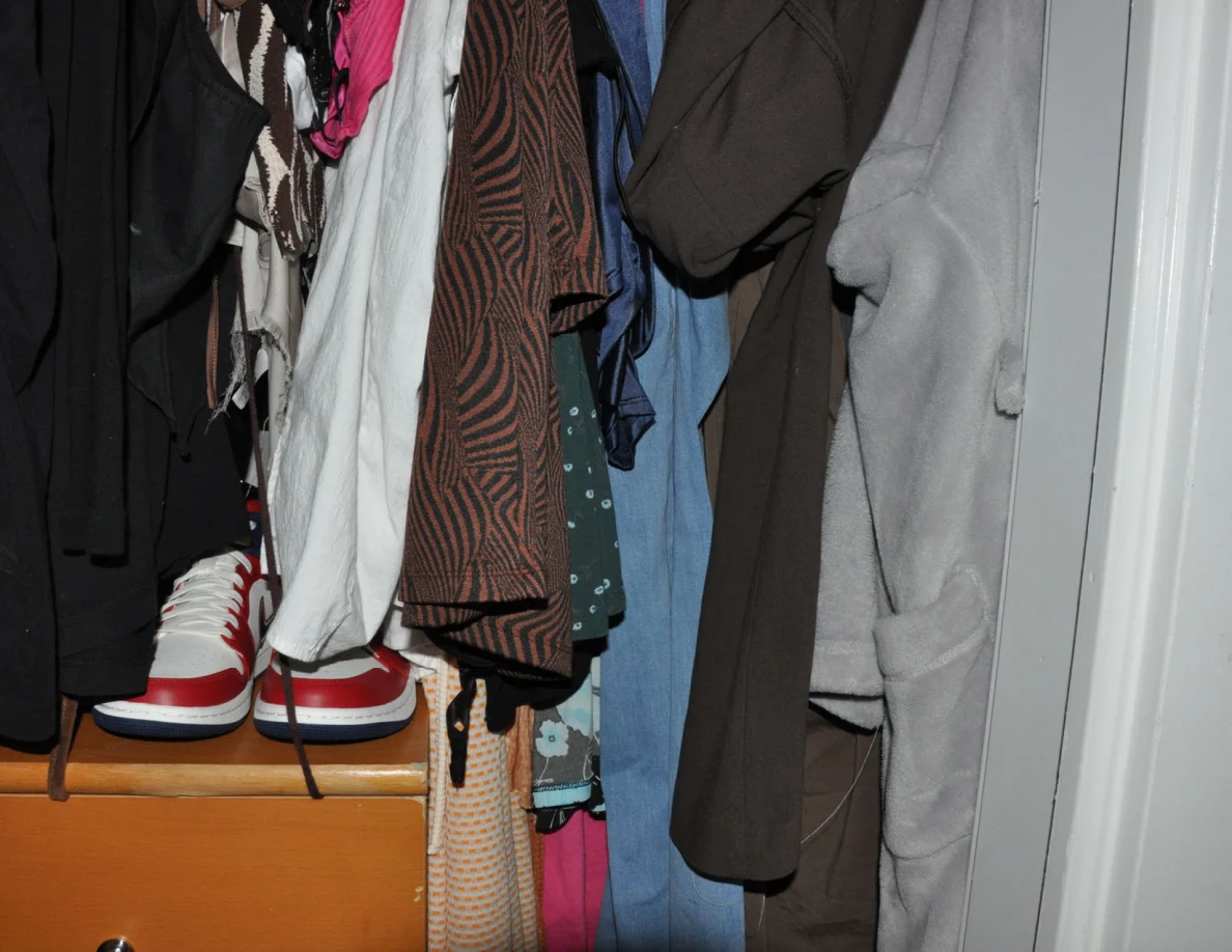 Hanging clothes and red-and-white shoes above a wooden drawer unit.
