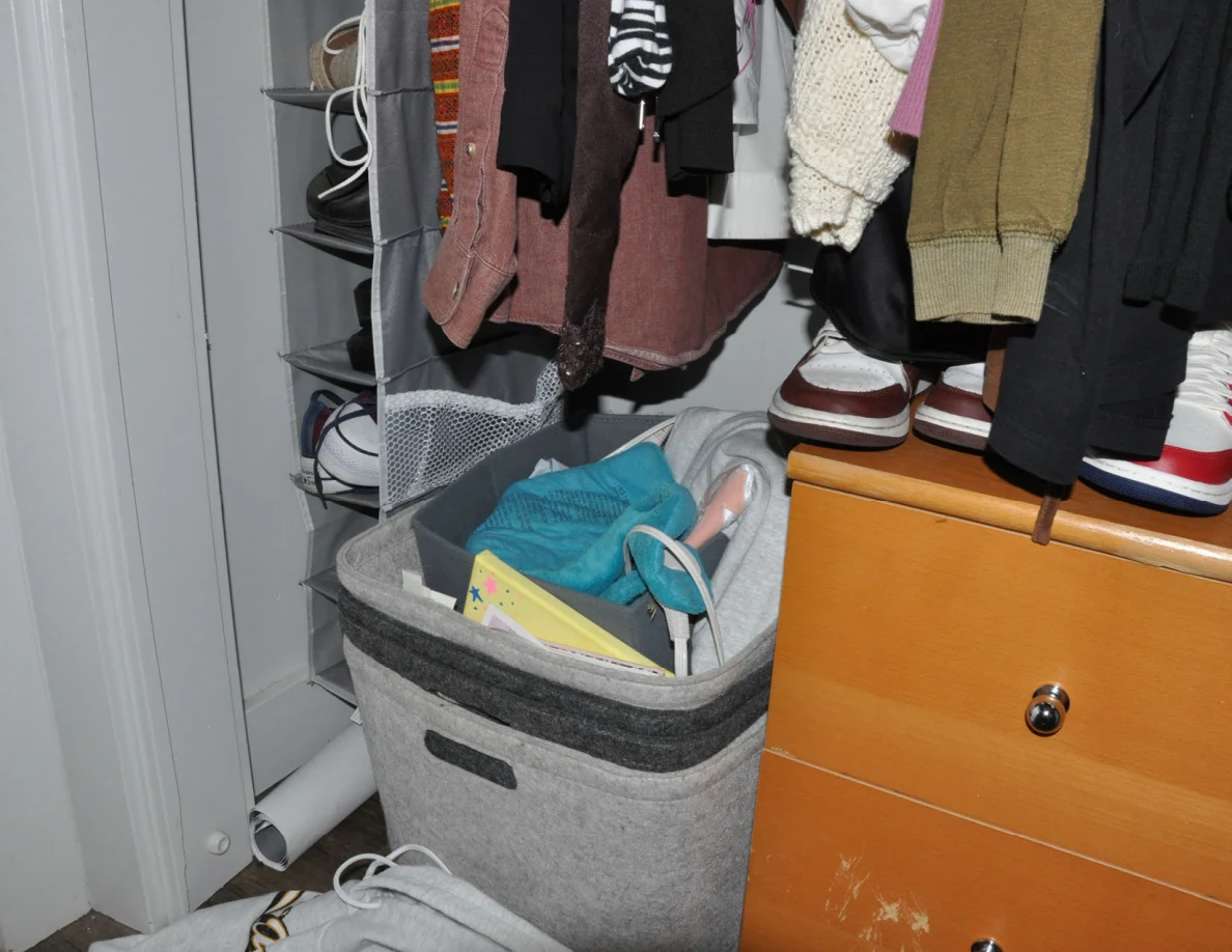 Gray basket filled with items beside wooden closet drawers and a hanging shoe organizer.