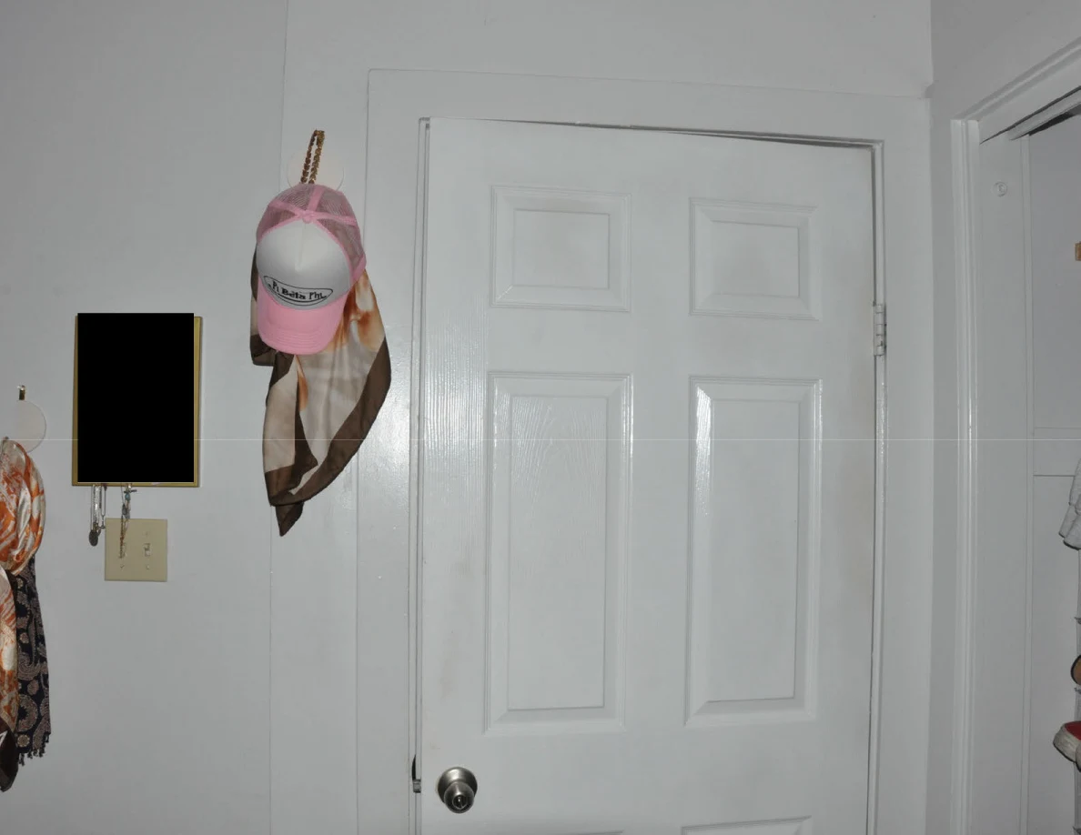 Upper closed bedroom door beside hanging hats and a scarf, with a redacted wall item.