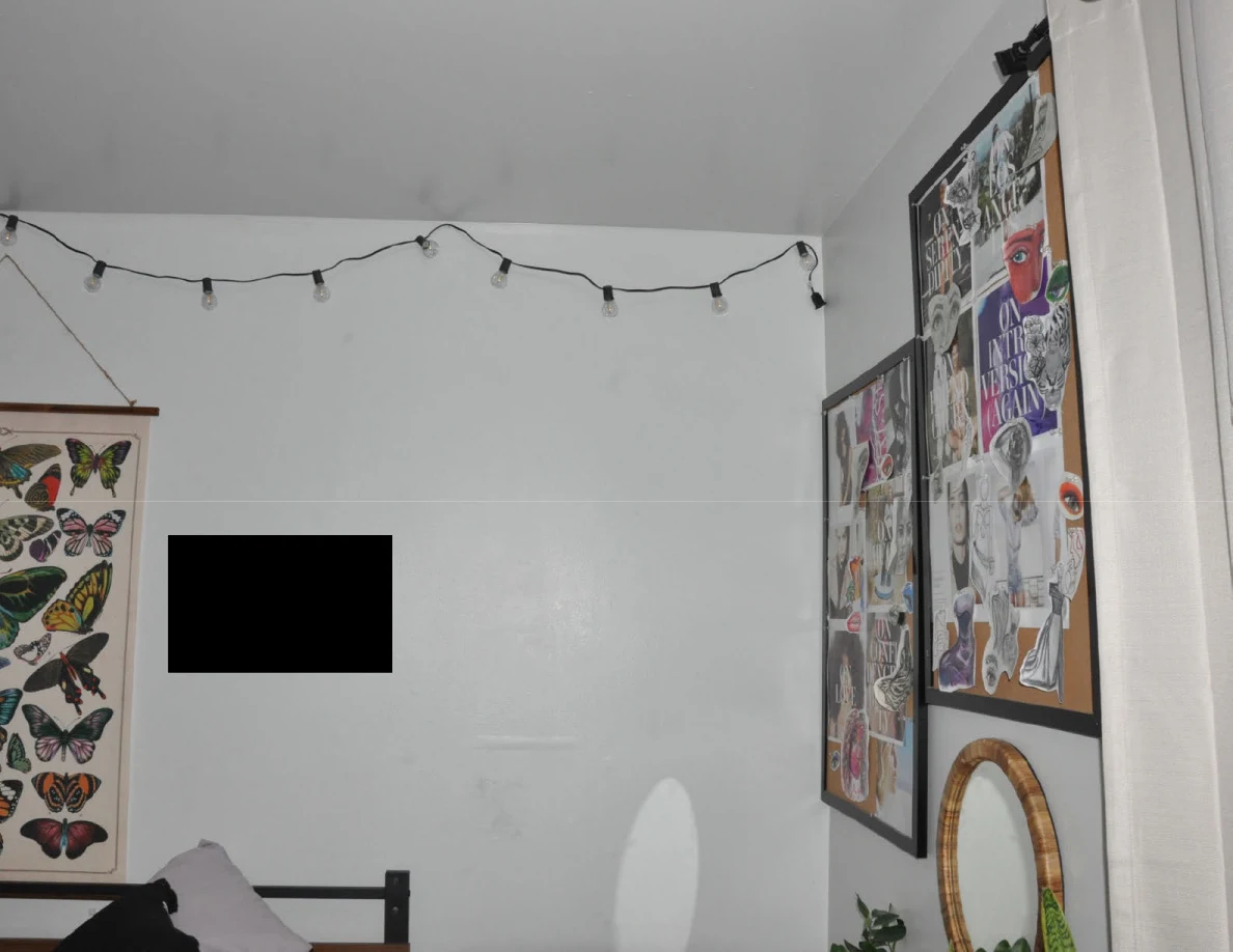 Upper bedroom corner with string lights, wall collages, round mirror and a black wall redaction.