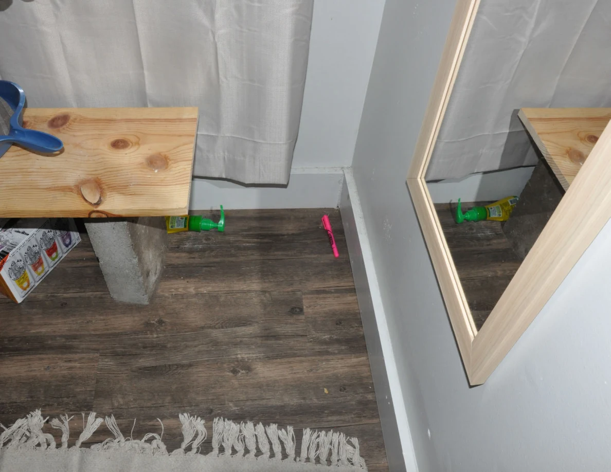 Lower wall mirror reflecting a wooden bench and curtain above floor objects.