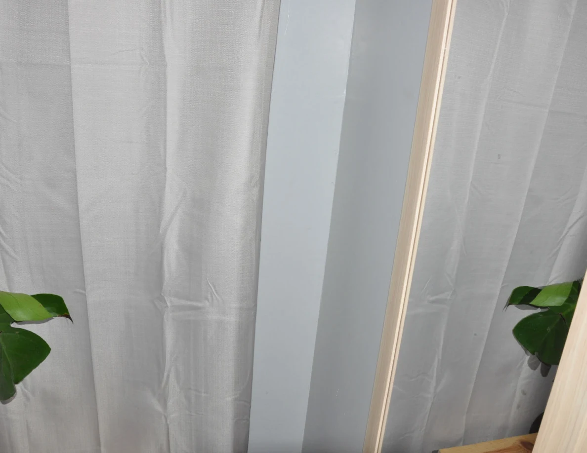 Narrow wall mirror beside white curtains and the edge of a plant.