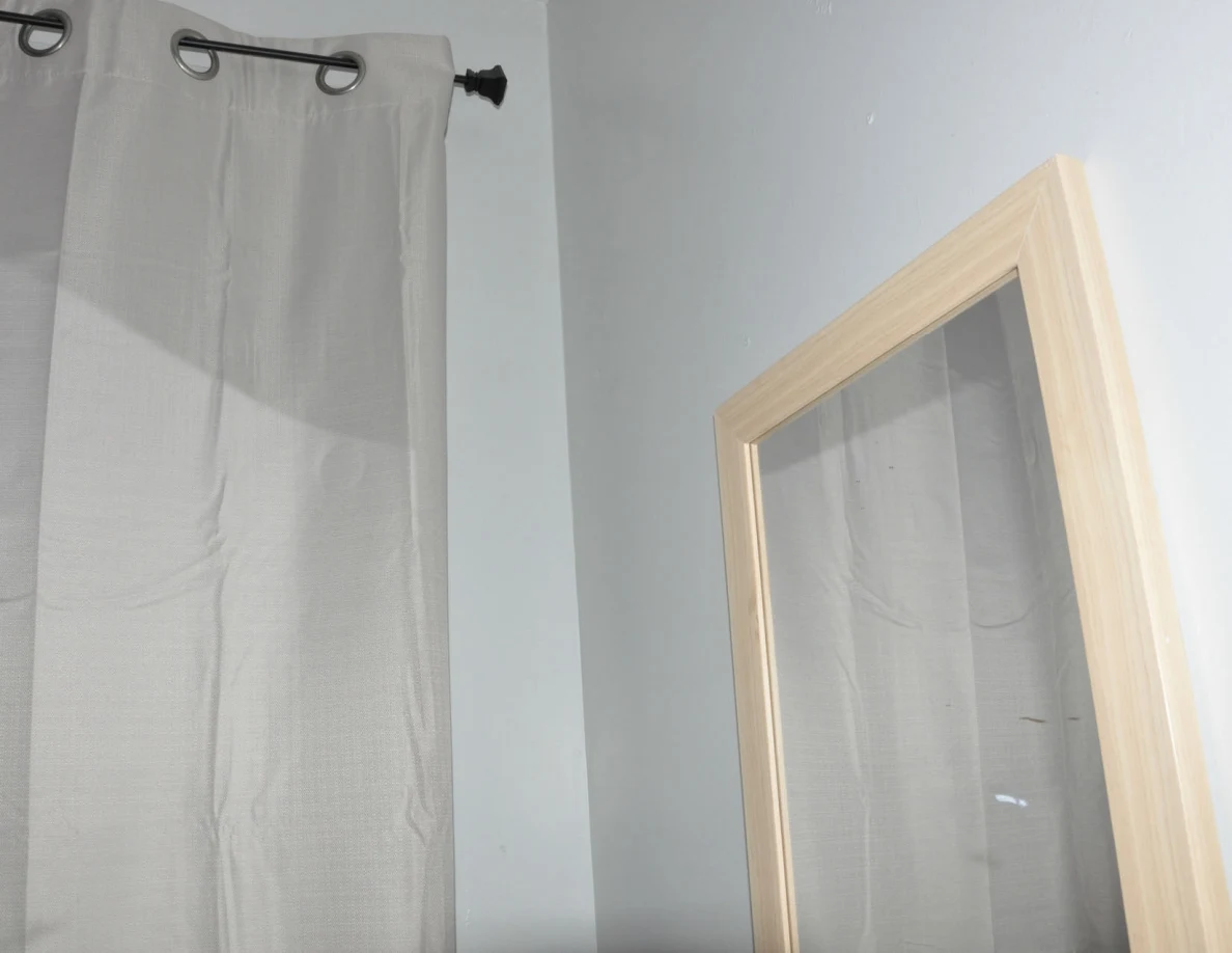 Upper wall mirror beside the end of a curtain rod.