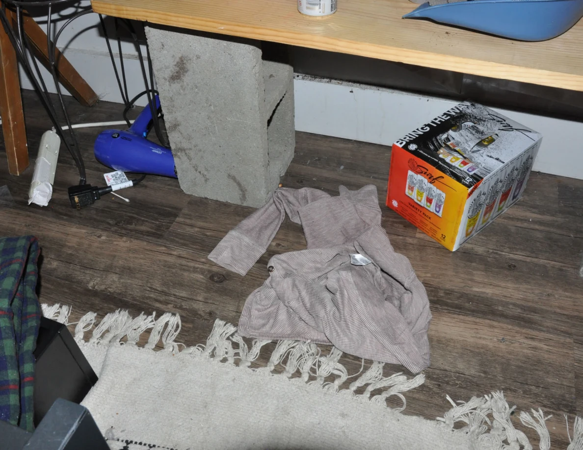 Floor beneath a concrete-block bench with a hair dryer, drink carton, loose fabric and rug fringe.