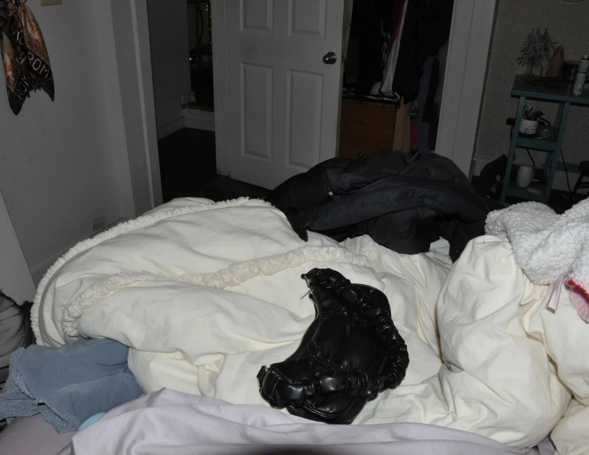 Rumpled bed with a black bag and dark jacket, facing an open door and closet.