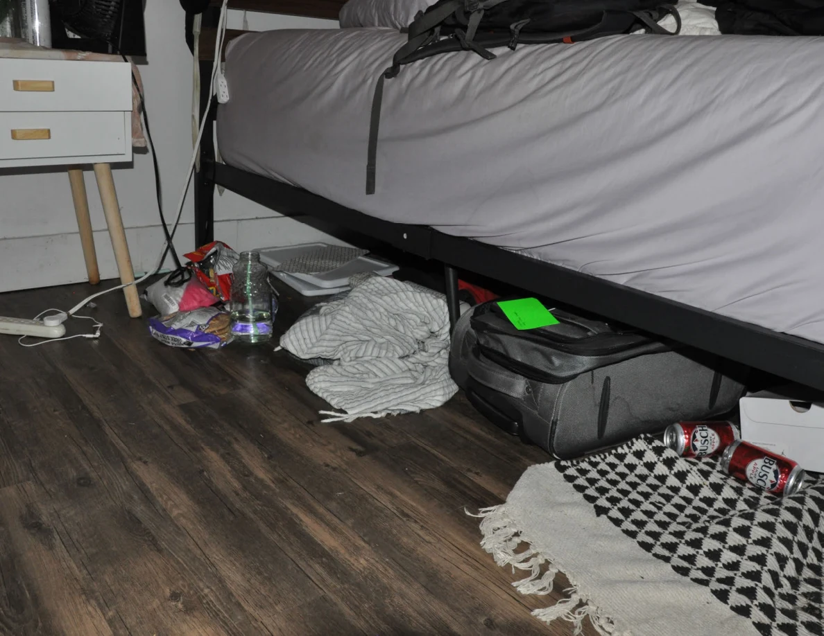 Side of bed above a gray storage bag, drink cans, striped fabric and snack packaging.