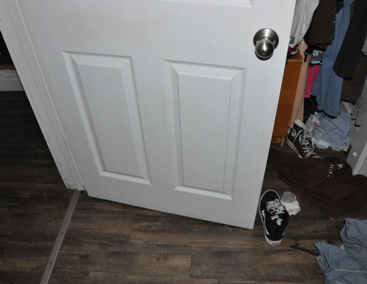 Lower open white door with round knob beside closet clothing and shoes.