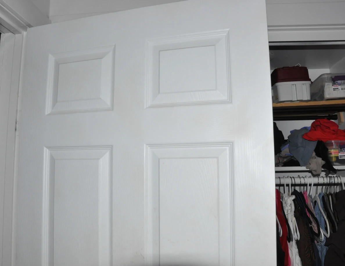 Upper white paneled door in front of closet shelves and hanging clothing.