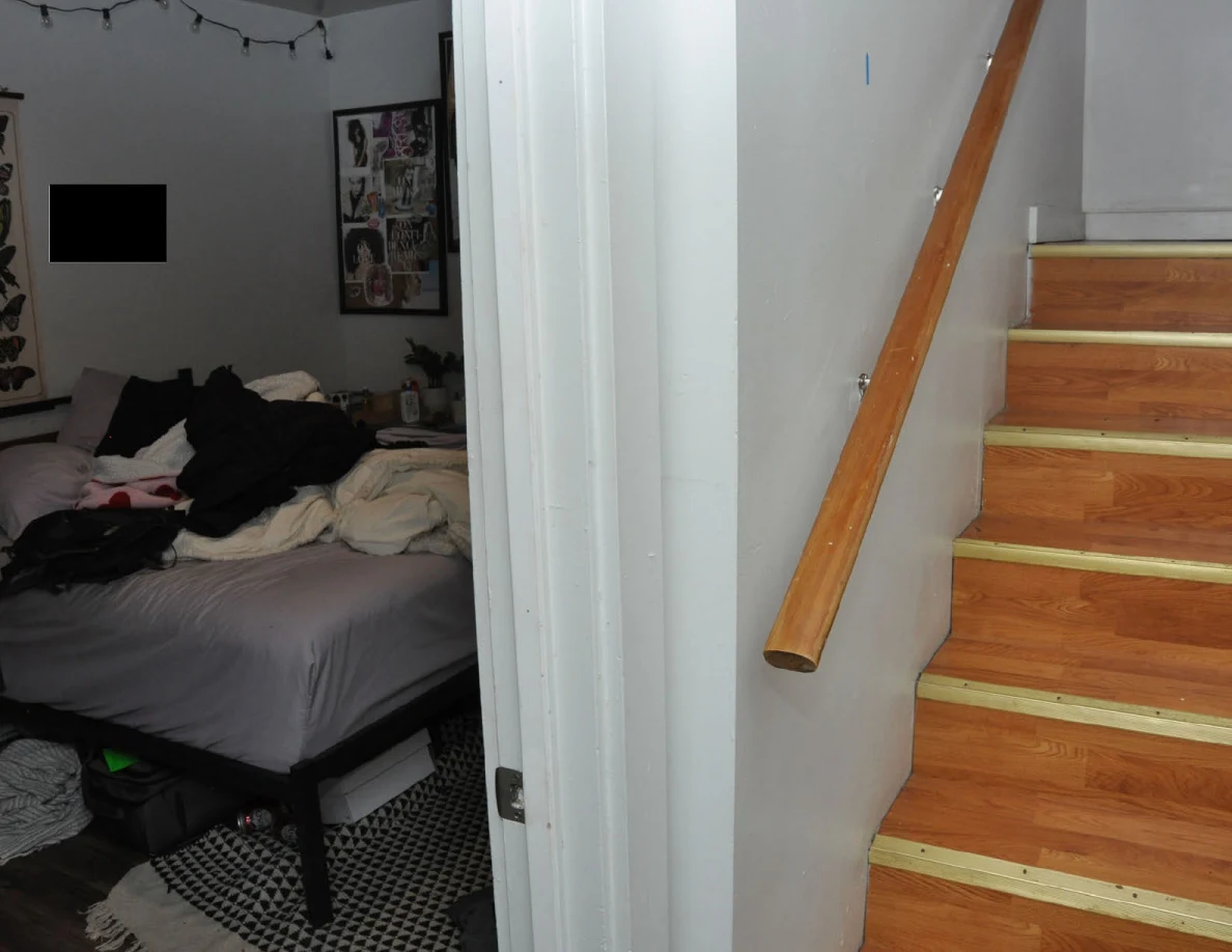 Bedroom doorway and bed beside a wooden stairway with handrail.